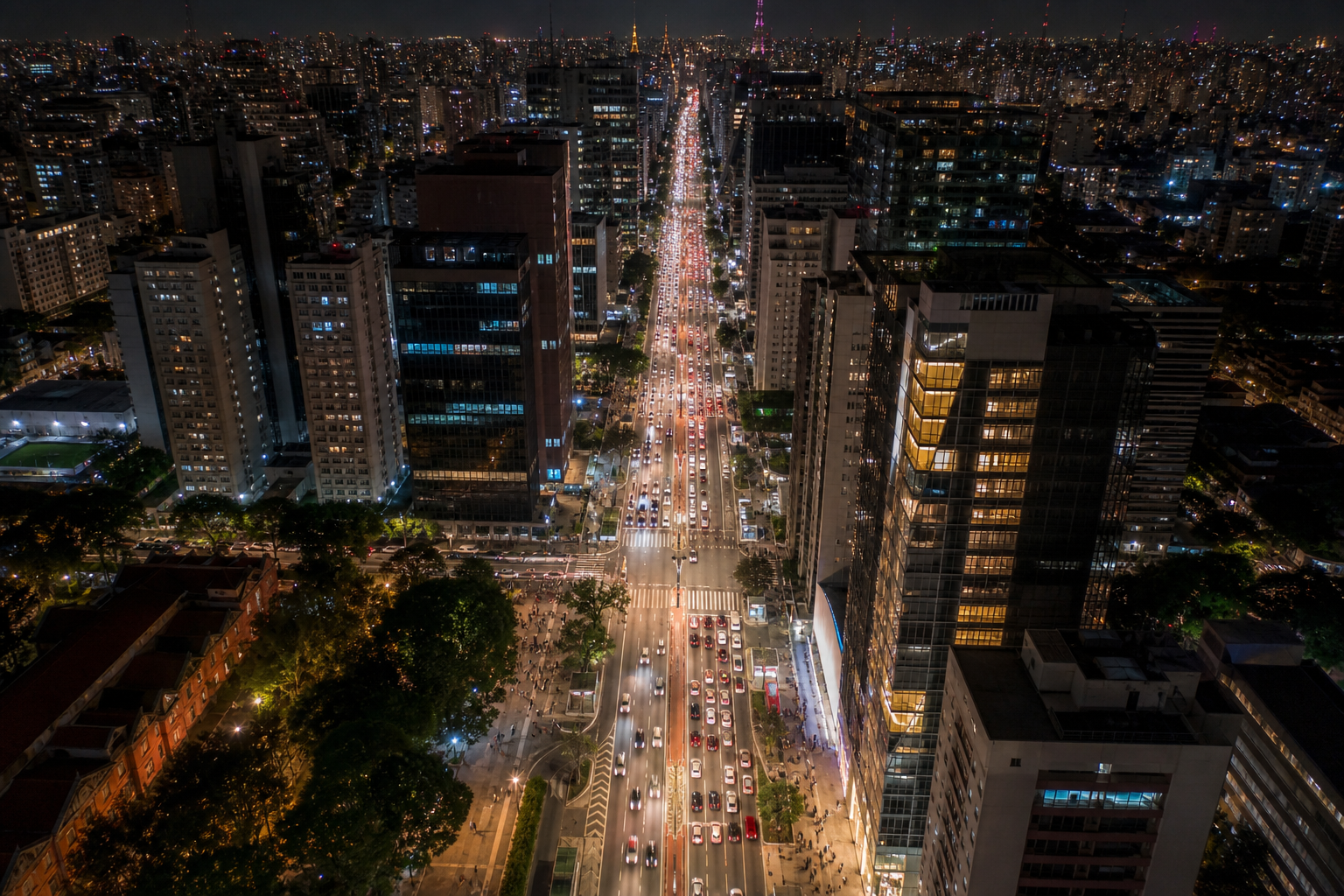 Vista noturna aérea da Avenida Paulista com prédios corporativos e fluxo intenso de veículos